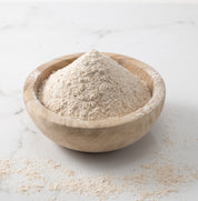 A woden bowl of freshly-milled rouge de bourdeaux wheat flour on a white marble slab with flour scattered on surface.