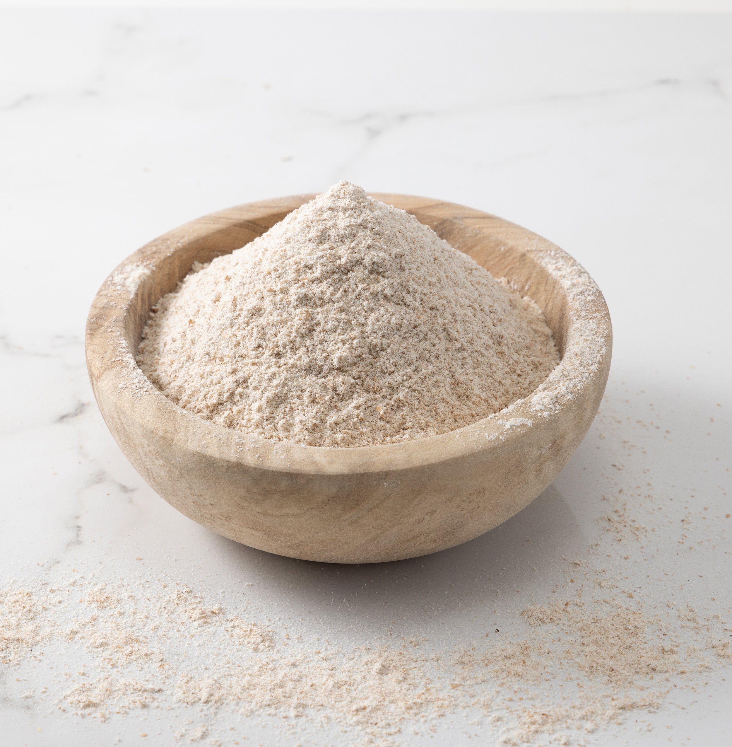 A woden bowl of freshly-milled rouge de bourdeaux wheat flour on a white marble slab with flour scattered on surface.