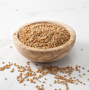 A wooden bowl filled with rouge de bourdeaux whole wheat grains, with a few scattered on a light marble surface.