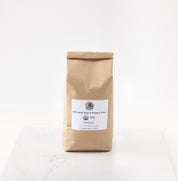 A brown kraft paper bag of rouge de bourdeaux wheat standing upright on a white marble surface against a white background.