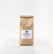 A brown kraft paper bag of streaker hulless oats featuring a white label with the brand logo, set on a white marble surface against a white background.