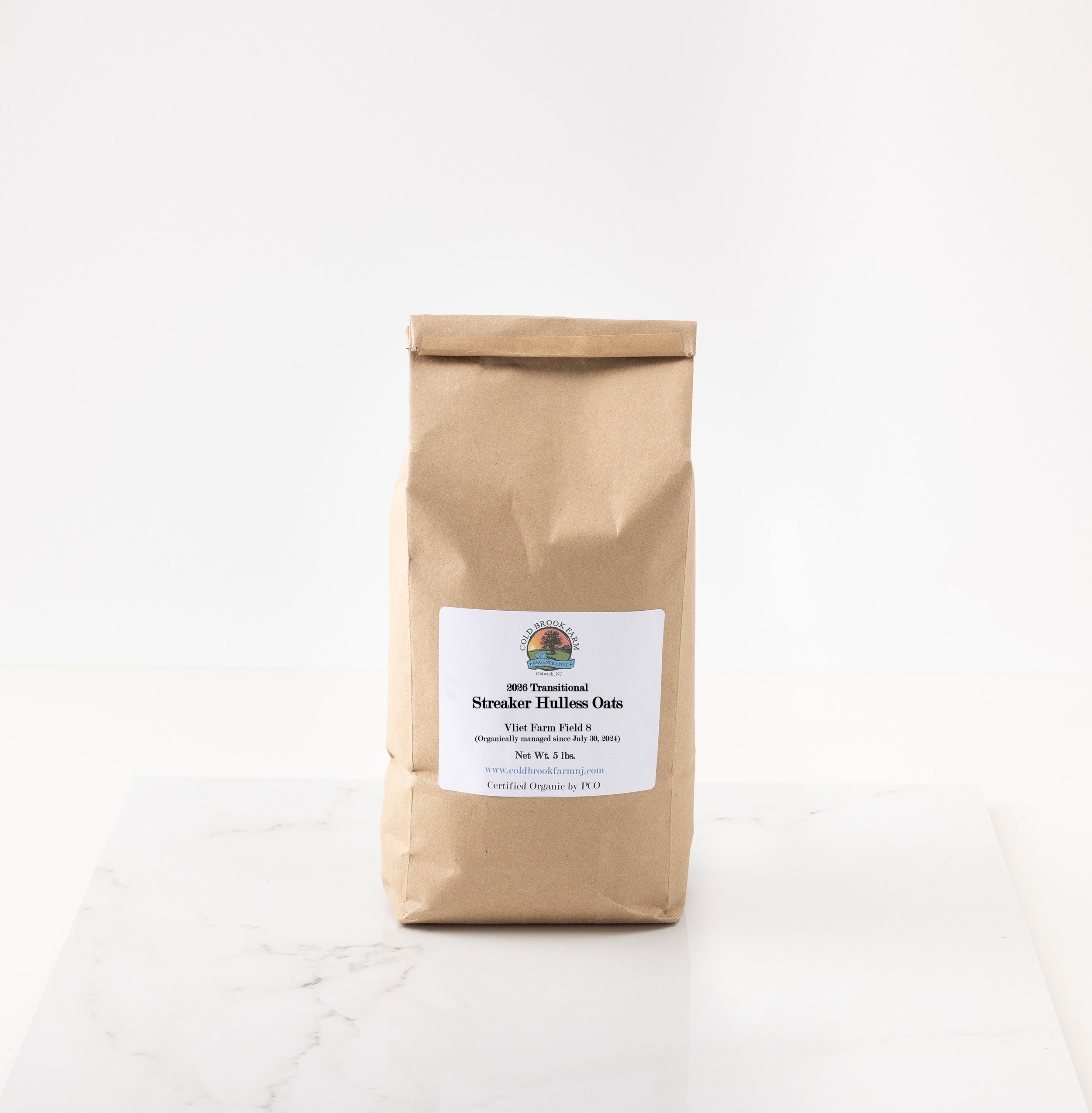 A brown kraft paper bag of streaker hulless oats featuring a white label with the brand logo, set on a white marble surface against a white background.