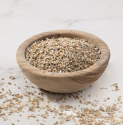 A small round wooden bowl filled with danko rye porridge, set on a light marble-like surface with some pieces scattered around.