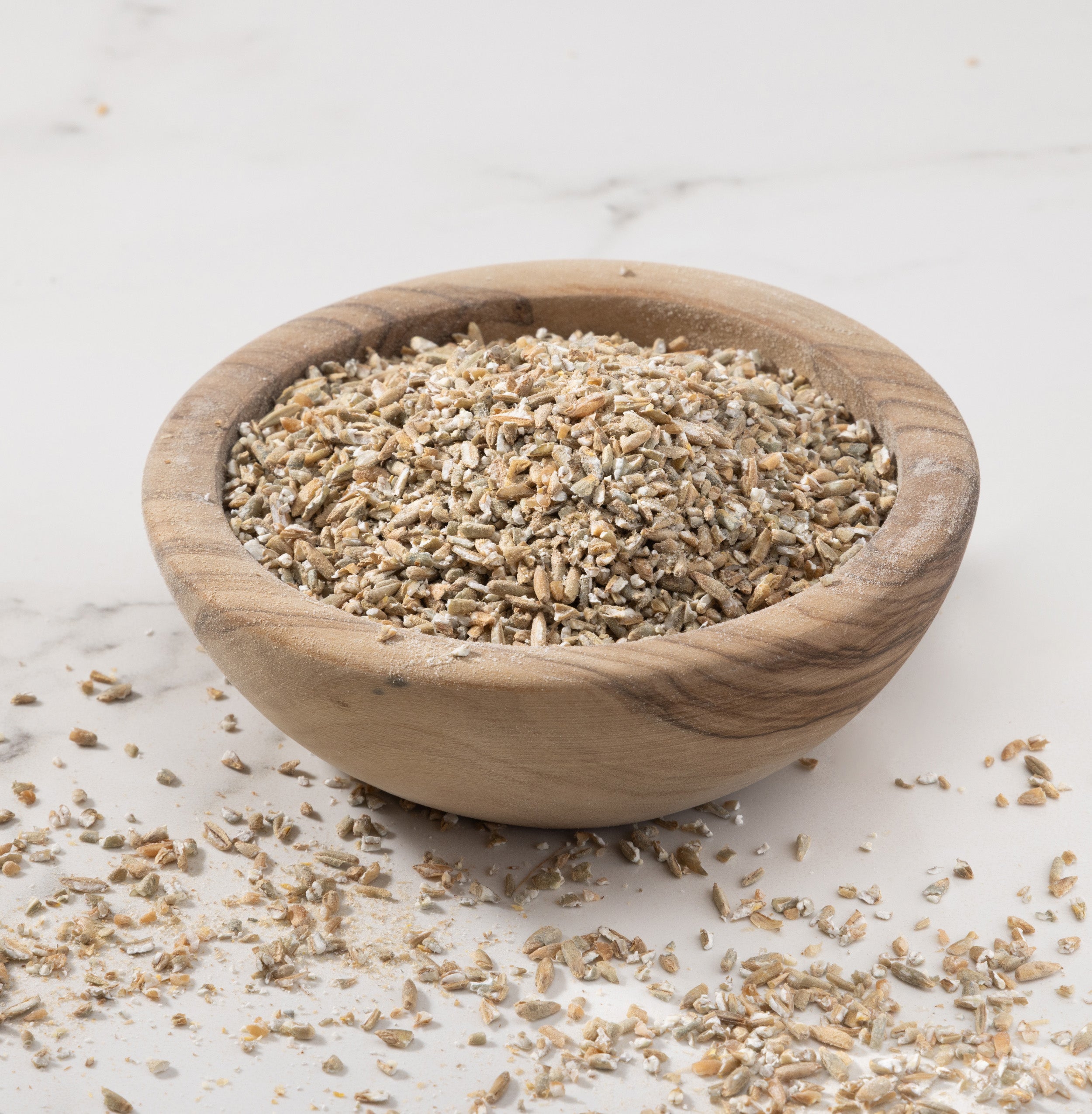 A small round wooden bowl filled with danko rye porridge, set on a light marble-like surface with some pieces scattered around.