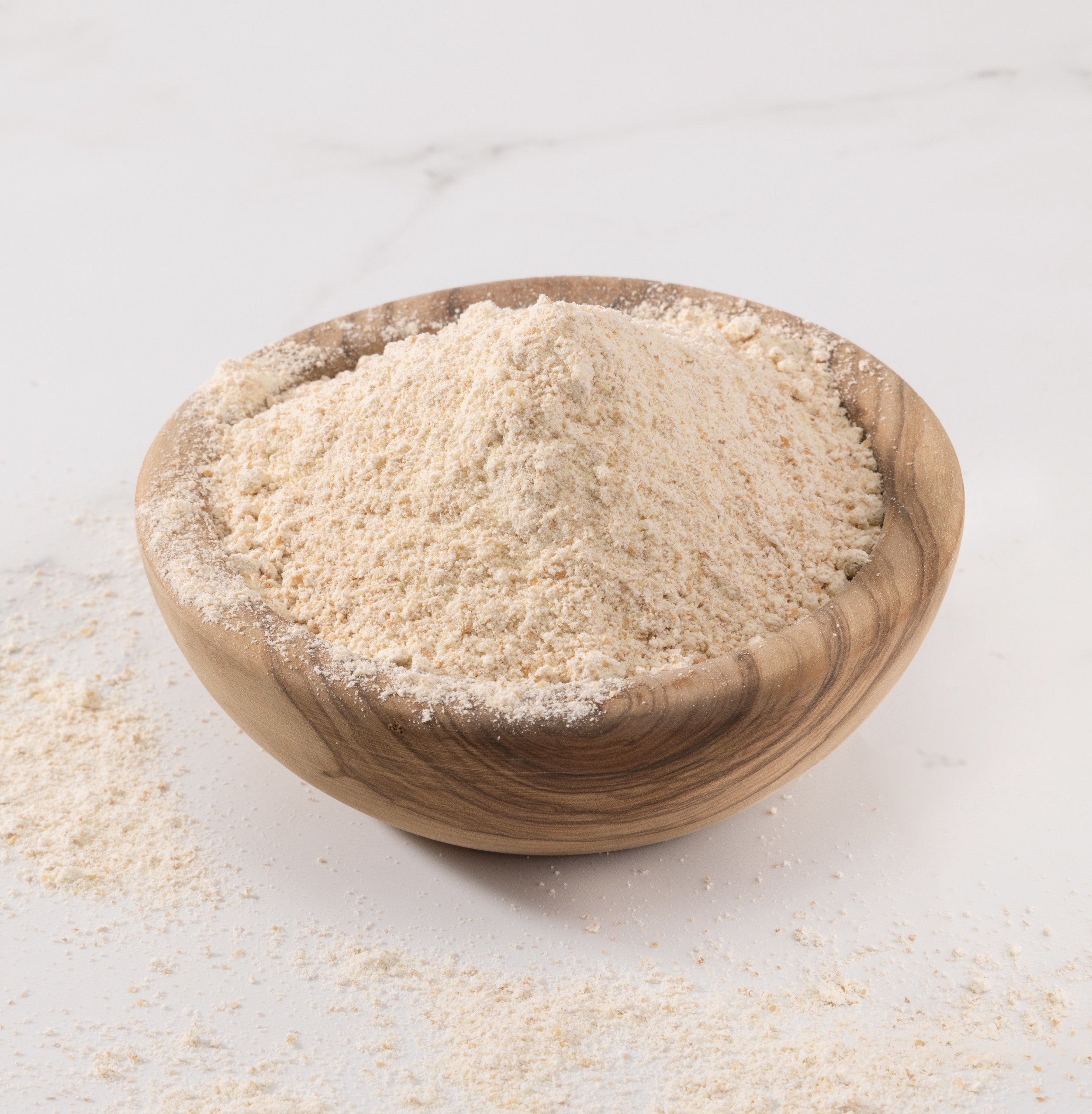 A mound of freshly-milled einkorn flour, displayed in a small wooden bowl on a light marble surface with some flour scattered around.