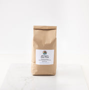 A brown kraft paper bag of 2026 Premium Glen Wheat Flour standing on a white marble surface against a white background.