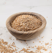 A small round wooden bowl filled with glenn wheat porridge photographed on a light marble-like surface with some crumbs scattered around.
