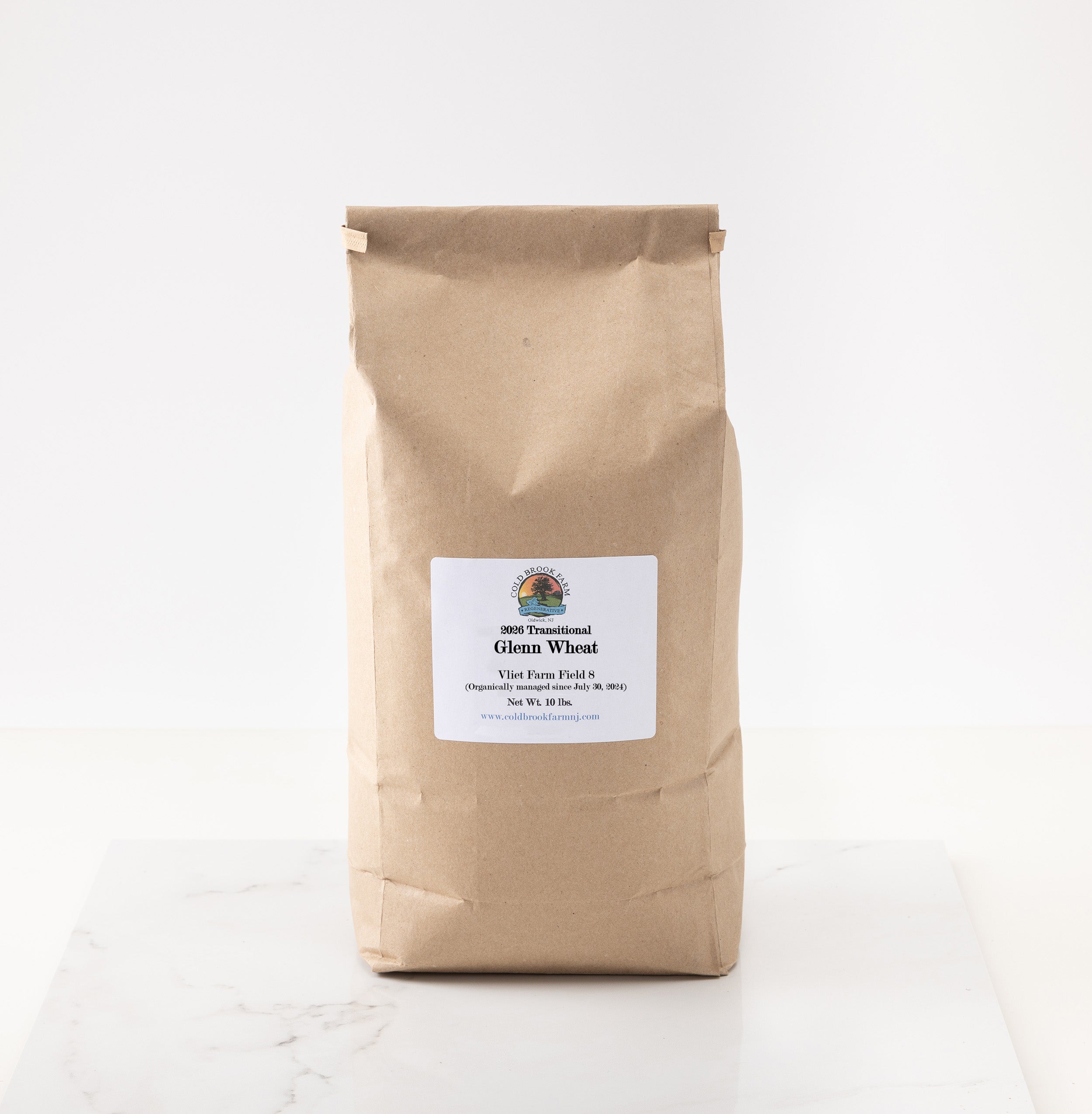 A brown kraft paper bag of 2026 glenn wheat displayed on a white marble surface against a white background.