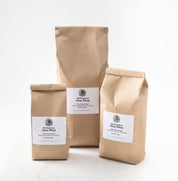 Three kraft paper bags of Glenn wheat berries in different sizes, arranged on a white surface against a white background.