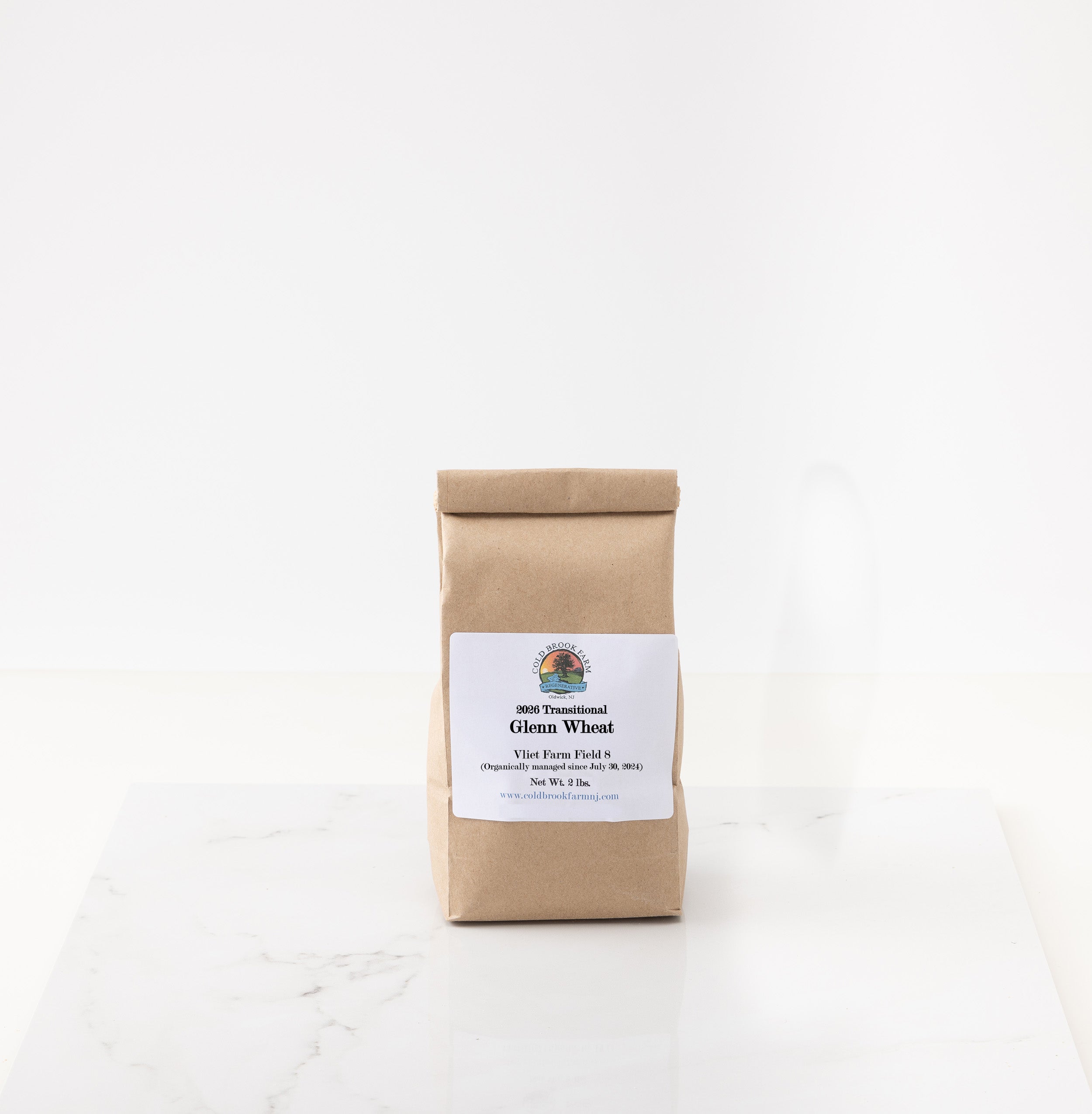 A brown kraft paper bag of 2026 glenn wheat standing upright on a white marble surface against a white background.