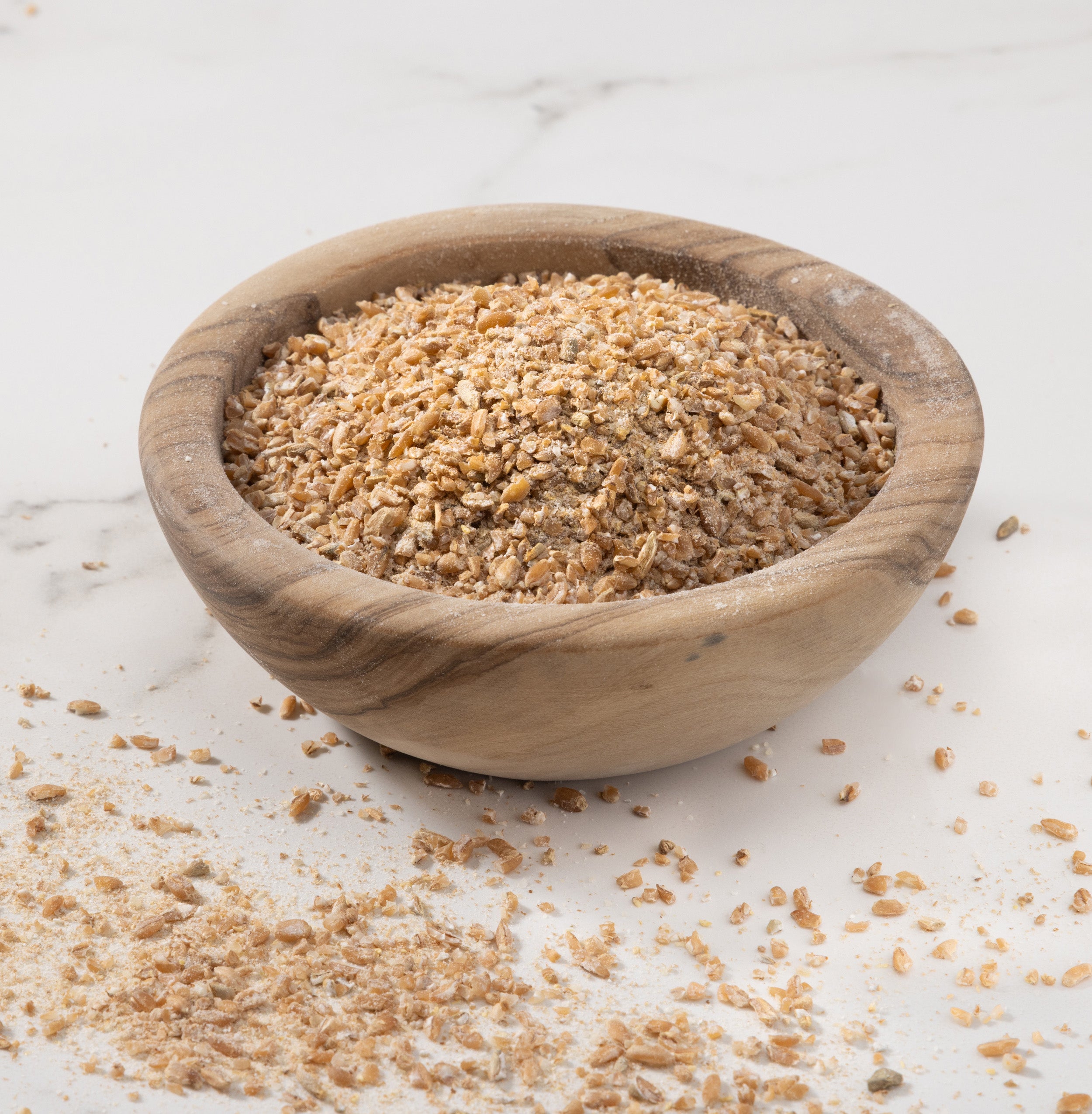 A small round wooden bowl filled with coarse cold brook farm backer's blend porridge set on a light marble-like surface with some sugar scattered around.