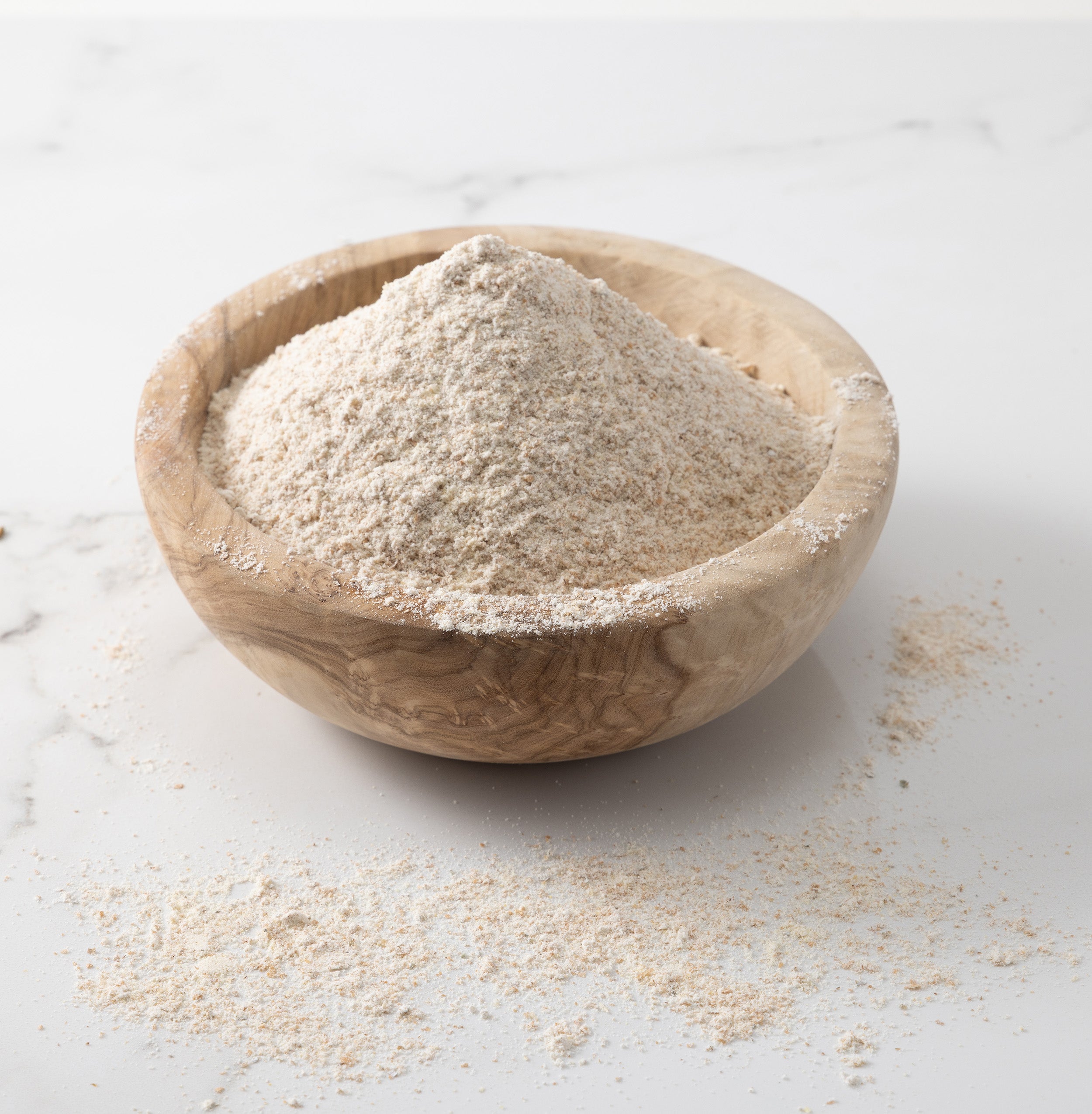 A woden bowl of freshly-milled baker's blend wheat flour on a white marble slab with flour scattered on surface.