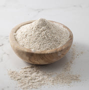 A woden bowl of freshly-milled danko rye flour on a white marble slab with flour scattered on surface.