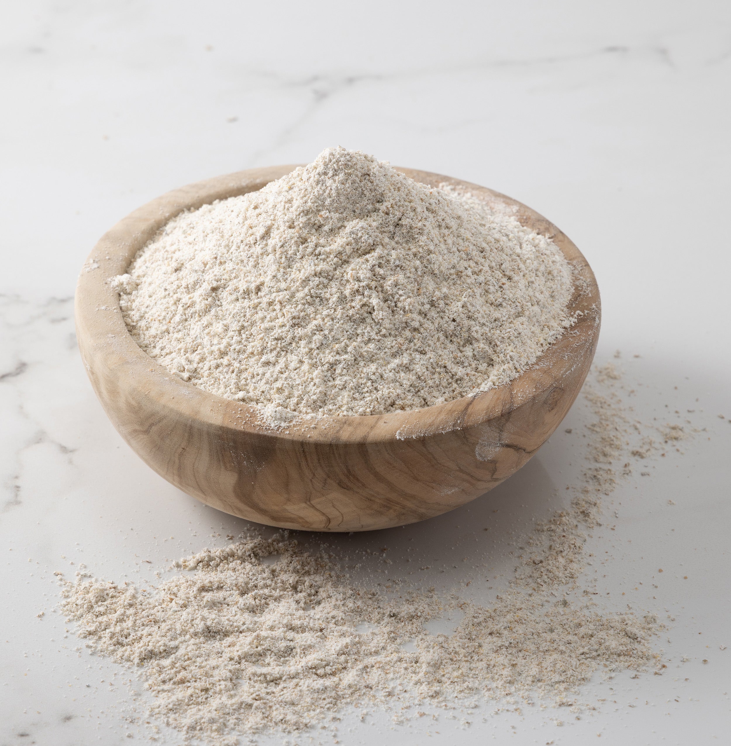 A woden bowl of freshly-milled danko rye flour on a white marble slab with flour scattered on surface.
