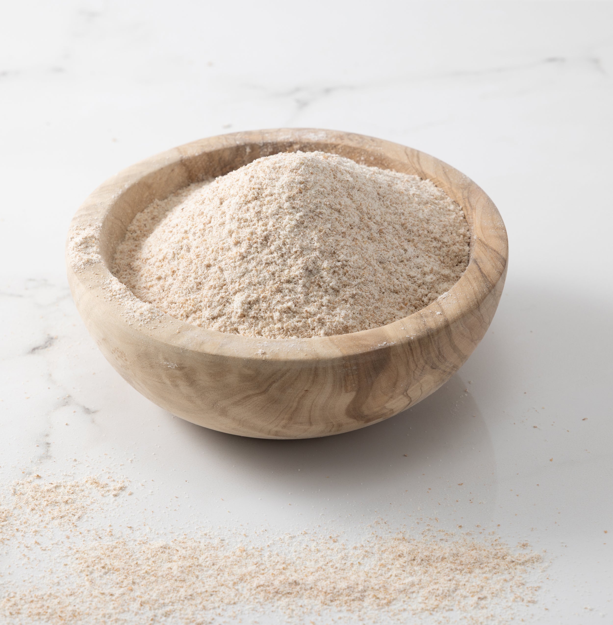 A woden bowl of freshly-milled glenn wheat flour on a white marble slab