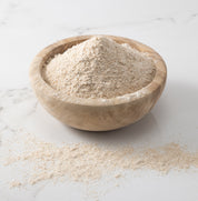 A woden bowl of freshly-milled redeemer wheat flour on a white marble slab with flour on surface.