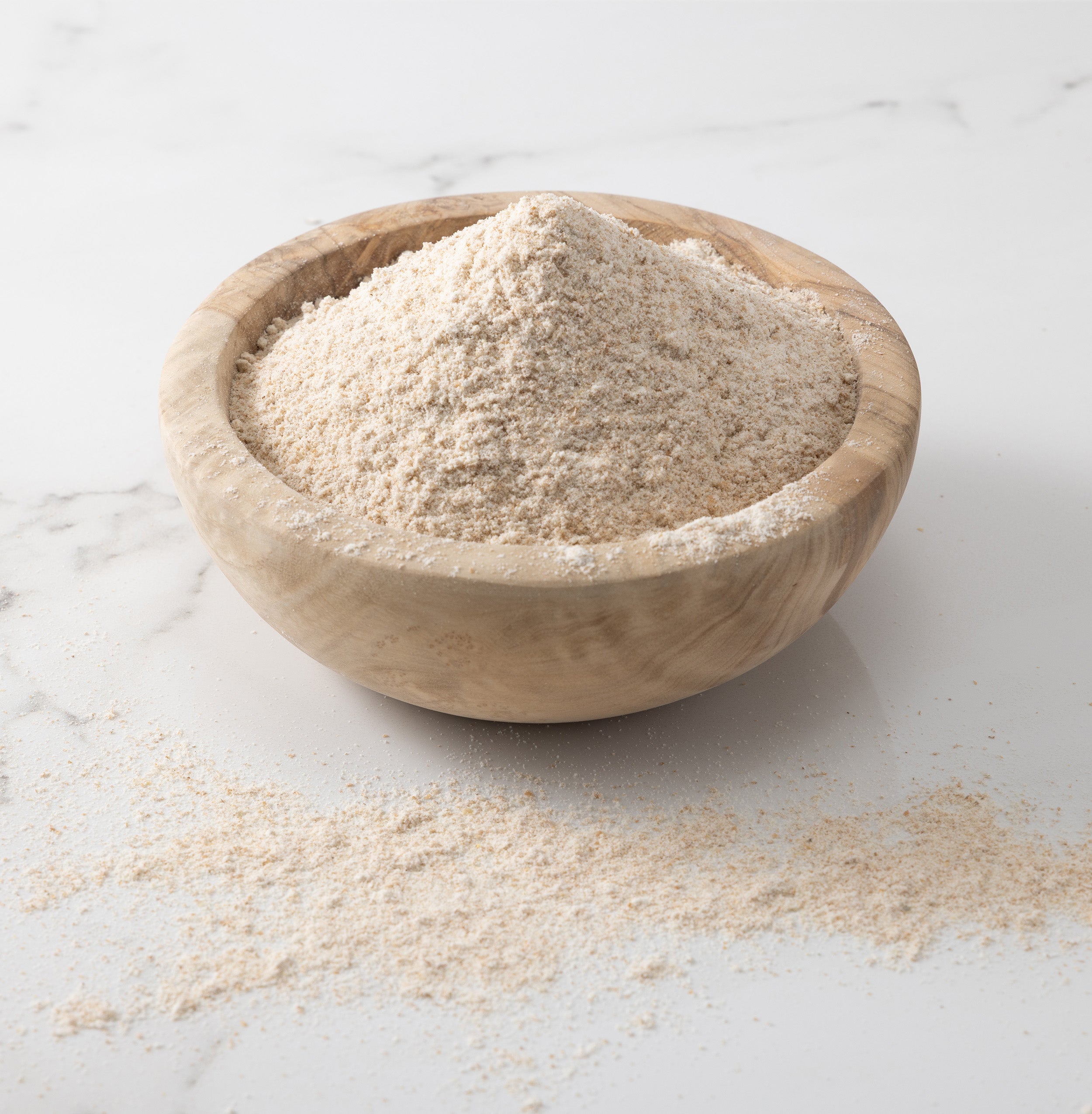 A woden bowl of freshly-milled redeemer wheat flour on a white marble slab with flour on surface.