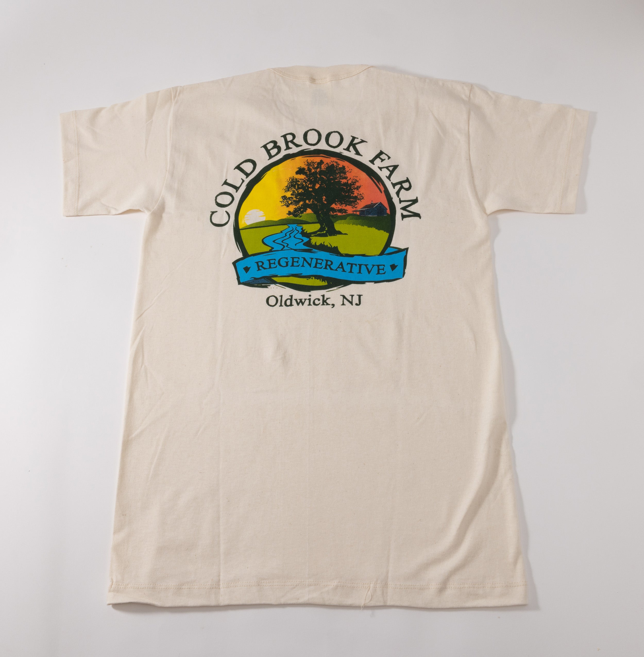 An off-white short-sleeve t-shirt laid flat against a light gray background, featuring a large vintage-style graphic on the back with the text 'COLD BROOK FARM', 'Oldwick, NJ', and a colorful farm landscape illustration.