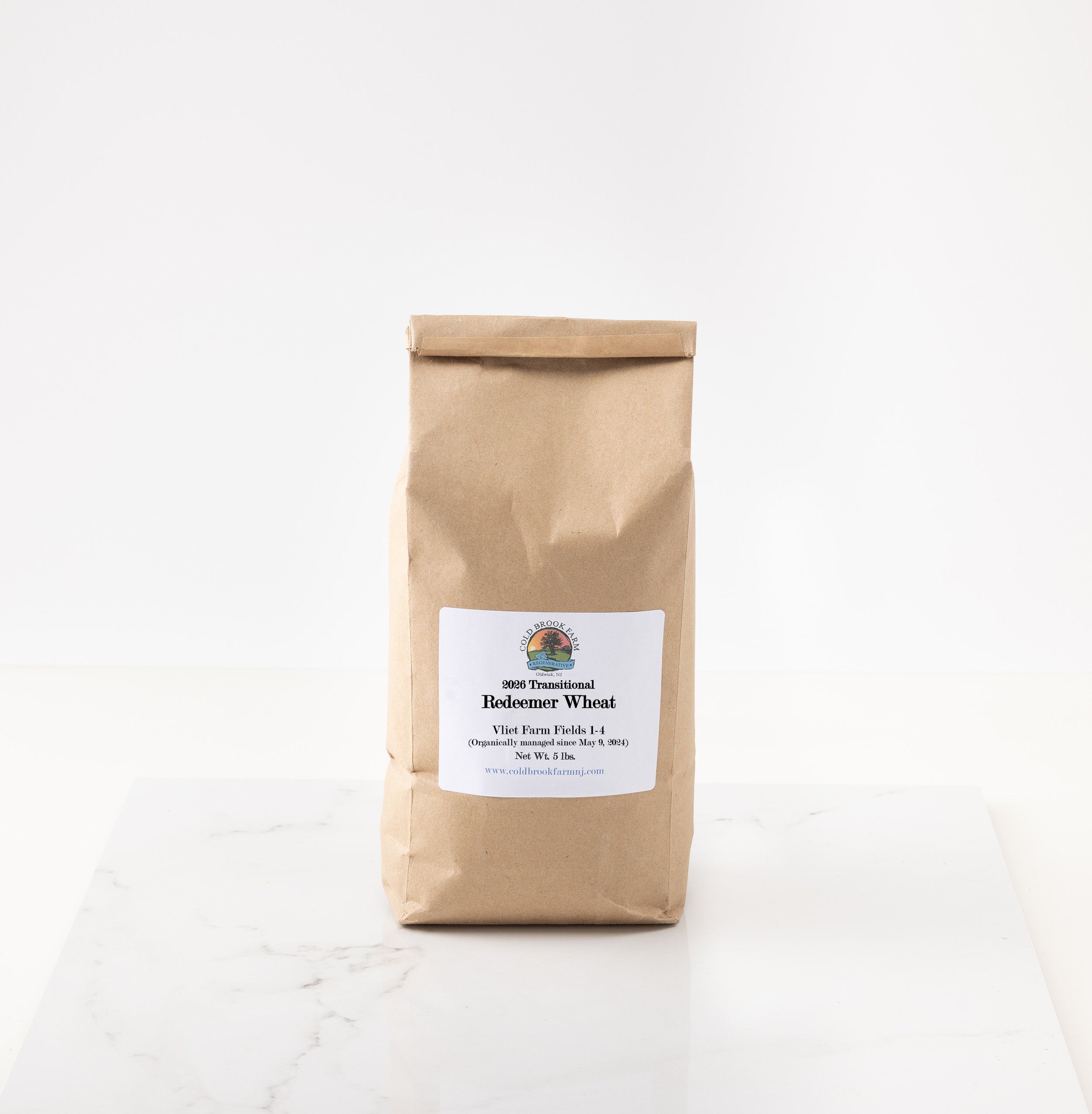 A brown kraft paper bag of 2026 redeemer wheat featuring a white label with the brand logo, set on a white marble surface against a white background.