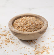 Redeemer wheat porridge grains in a small round wooden bowl, set on a white marble surface with some grains scattered around.